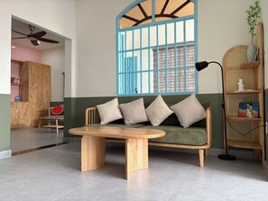Uma sala de estar moderna com um sofá de madeira, uma mesa de centro redonda, uma estante e uma janela grande com persianas azuis.