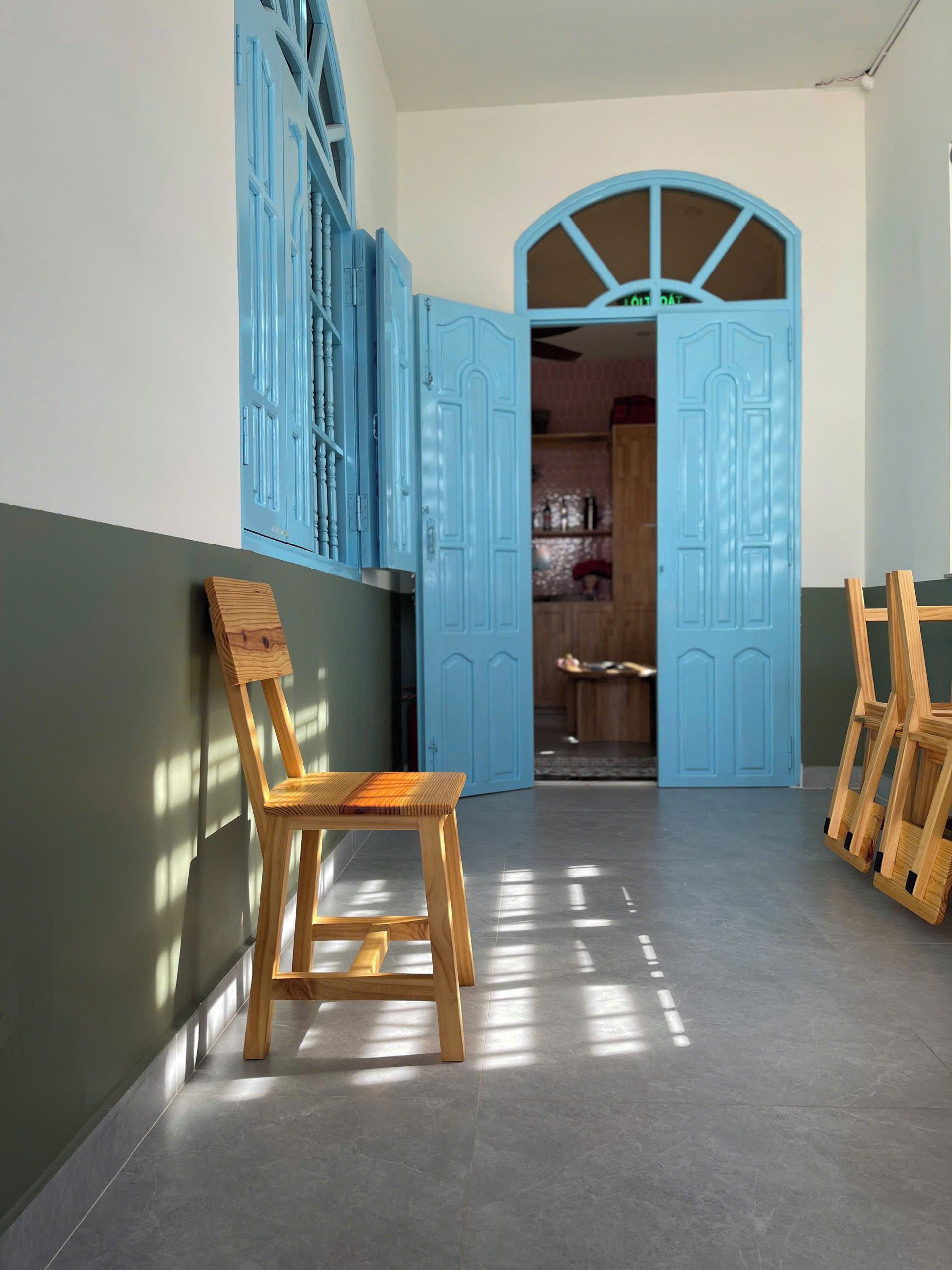Un pasillo con una silla de madera, puertas azules y suelo de baldosas.