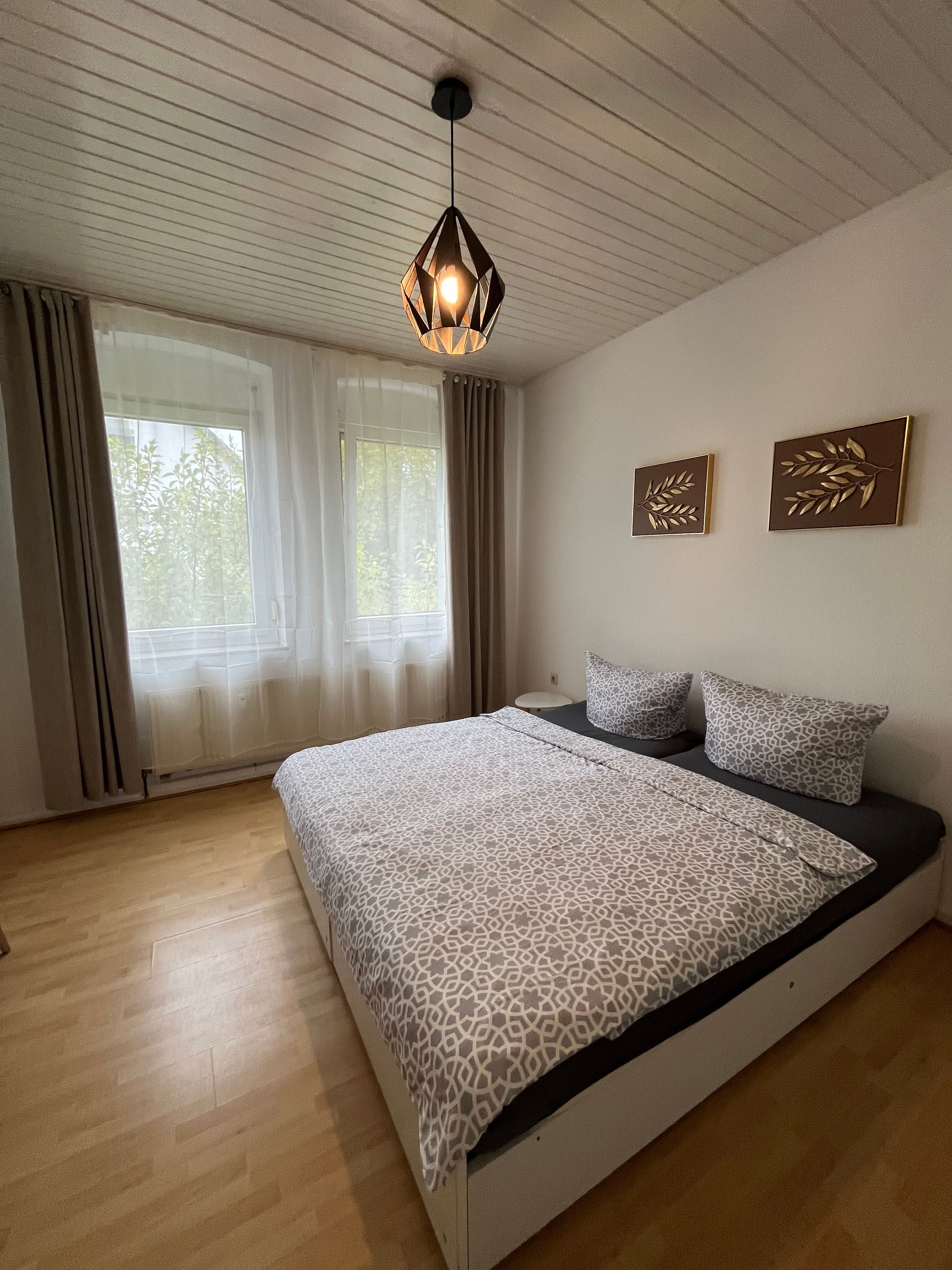 A bedroom with a bed, a hanging light fixture, two wall-mounted leaf-shaped decorations, and a window with curtains.
