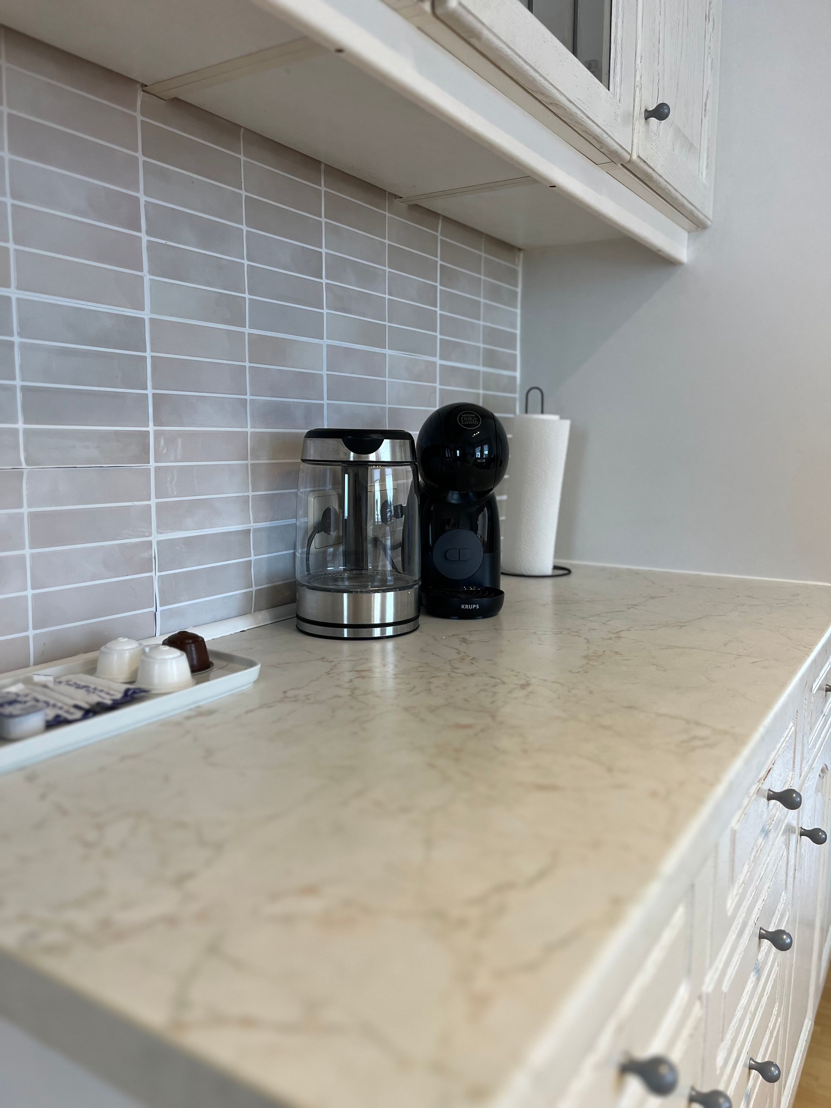 A kitchen counter with a coffee maker, a glass carafe, and a tray with eggs and a chocolate.