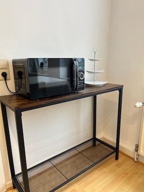 Eine schwarze Mikrowelle steht auf einem Holztisch, neben ihr ein weißes Tablett.