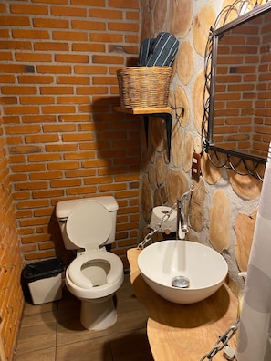 Un bagno con parete in mattoni, un water bianco, un lavandino in legno e un cesto su uno scaffale.