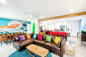 Een moderne woonkamer met een bruine leren bank, kleurrijke kussens, een houten salontafel en een levendige muurschildering.