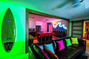 Un salon moderne avec un canapé en cuir noir, des coussins colorés et une décoration sur le thème du surf.