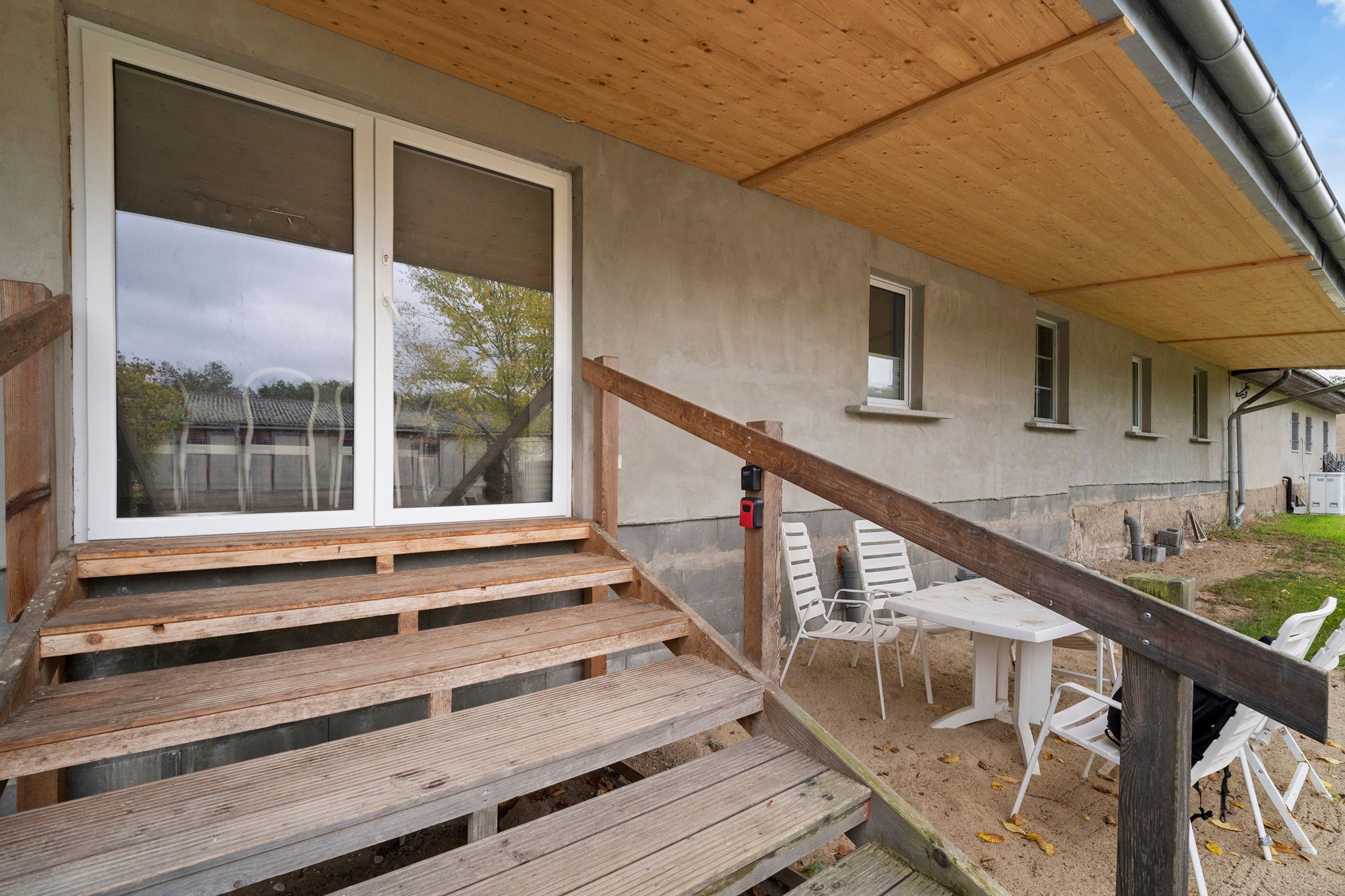 Un escalier en bois mène à un espace extérieur abrité, où se trouvent une table et des chaises.
