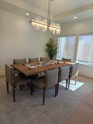 A dining area with a wooden table, six chairs, a hanging light fixture, and a potted plant. - Ocean-View Villa Jacuzzi Near Laguna Seca (Monterey)