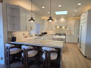 A modern kitchen with marble countertops, pendant lighting, and a central island with bar stools. - Ocean-View Villa Jacuzzi Near Laguna Seca (Monterey)