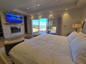 A bedroom with a large bed, a TV mounted on the wall, a fireplace, and a balcony with a view. - Ocean-View Villa Jacuzzi Near Laguna Seca (Monterey)