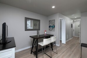 Uma sala de jantar moderna com mesa de madeira escura, cadeiras brancas, televisão de tela plana e um vaso decorativo.