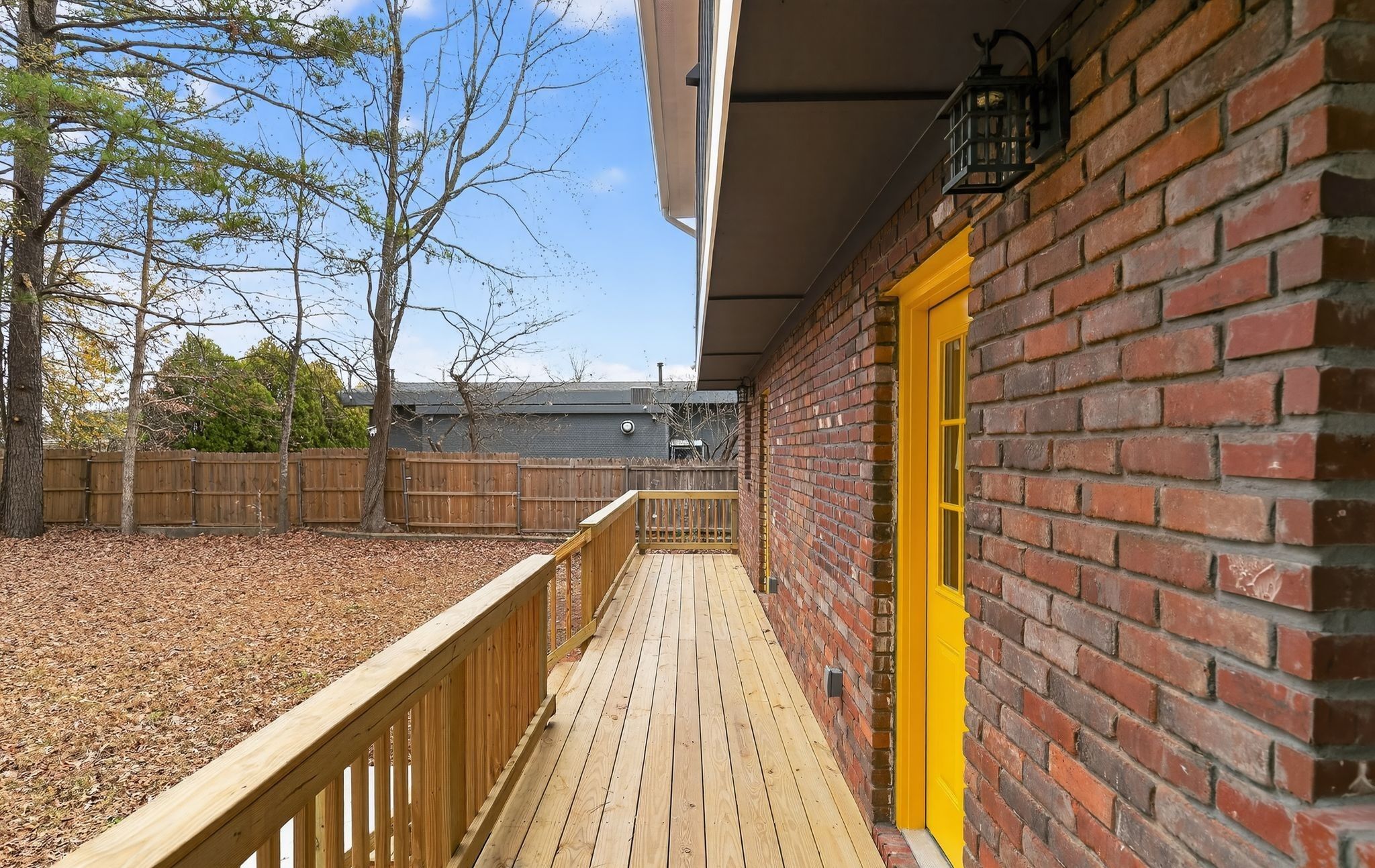 A wooden deck with a yellow door, brick wall, and a wooden fence.