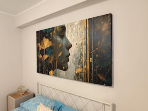 Ein Schlafzimmer mit einem Bett, einem Nachttisch und einem großen abstrakten Gemälde an der Wand.