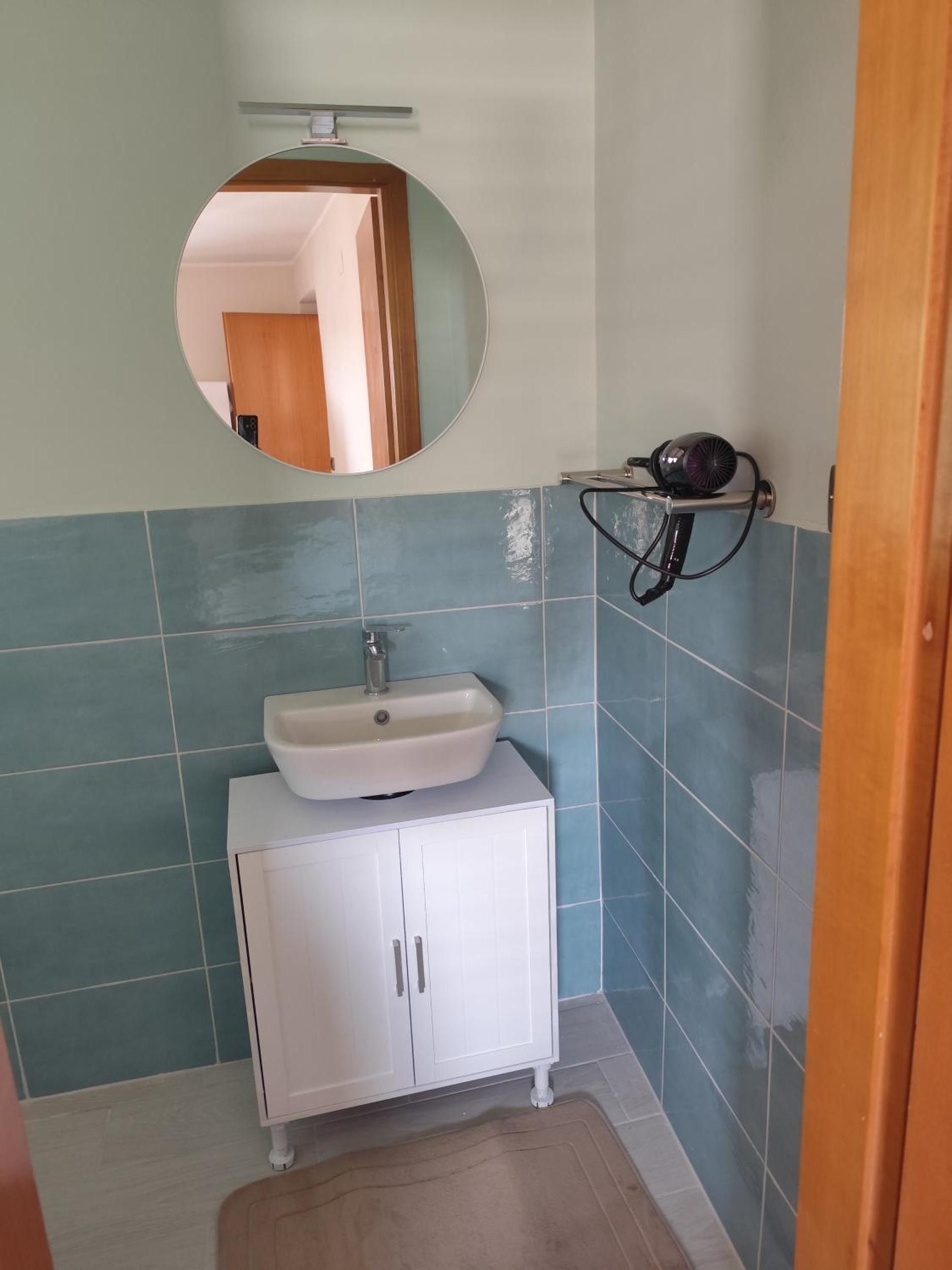 A bathroom with a round mirror, a sink, and a hairdryer on a shelf.