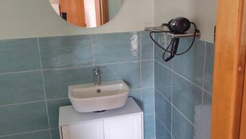 A bathroom with a round mirror, a sink, and a hairdryer on a shelf.