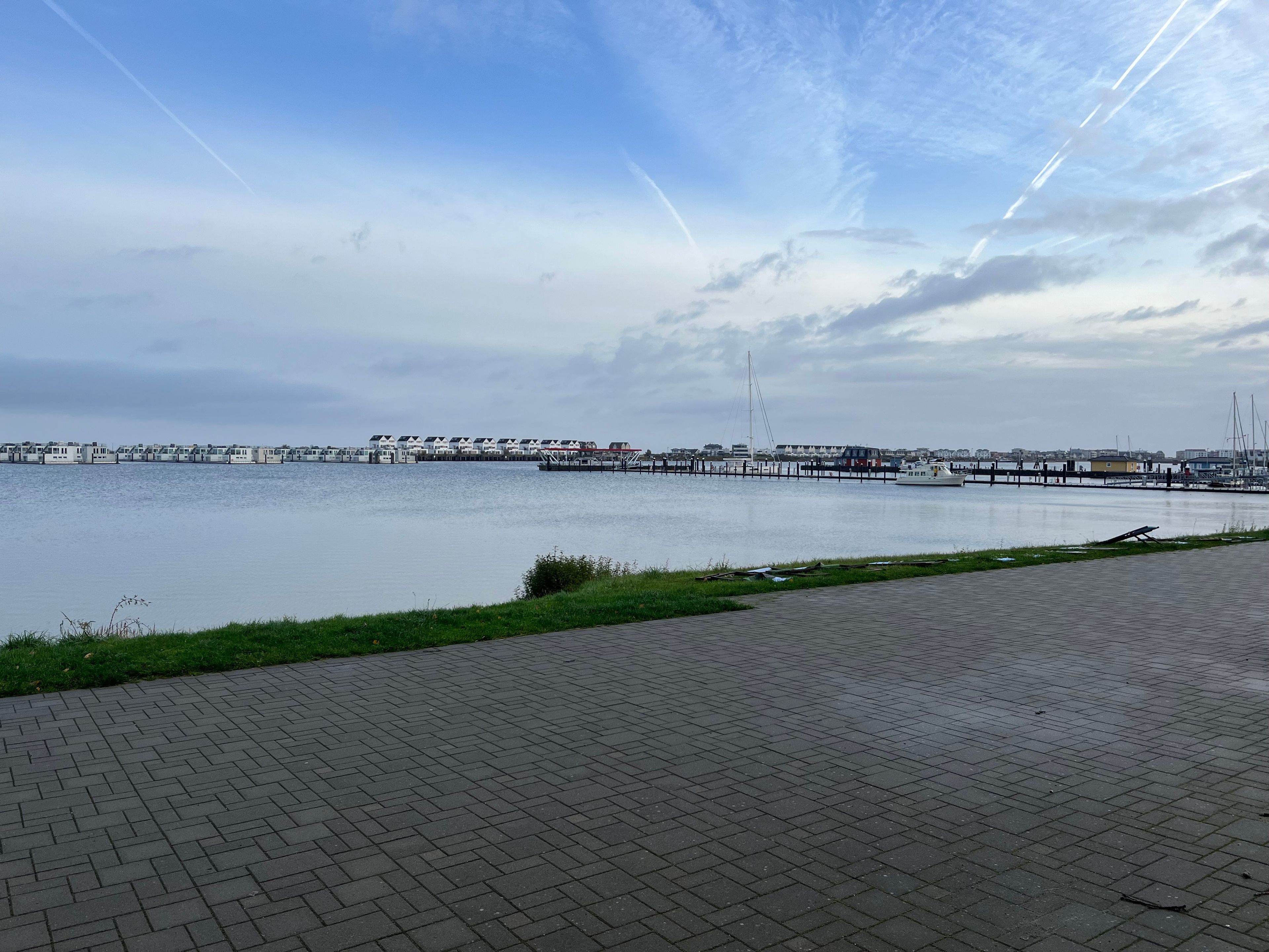 A waterfront promenade with a paved walkway, a row of buildings, and a body of water.