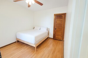 Una cama individual en una habitación con piso y puerta de madera.