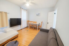 Una habitación con cama, sofá, televisión, ventilador de techo, mesa de comedor y sillas, y una puerta.