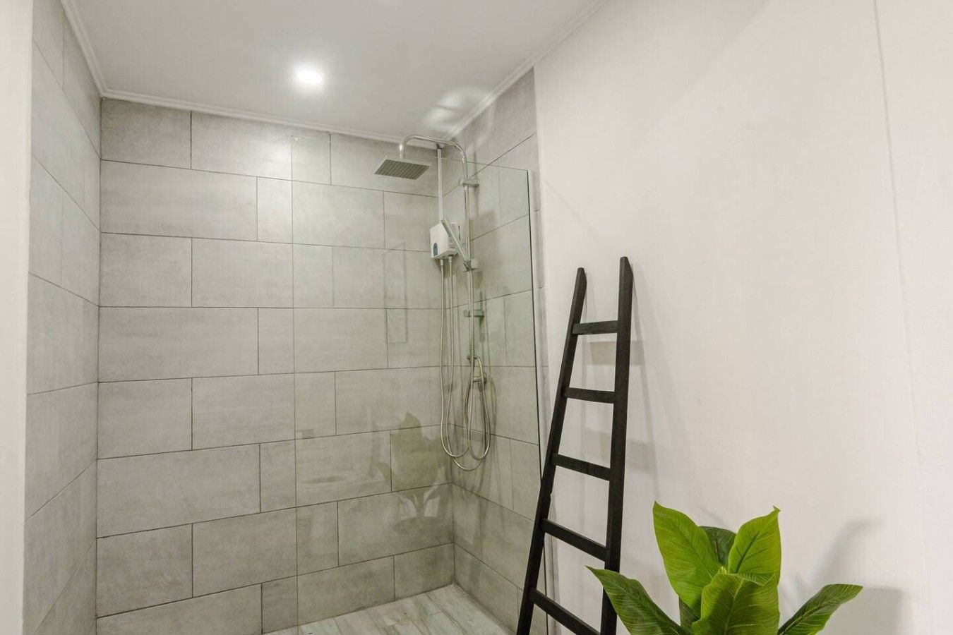 A shower area with tiled walls, a showerhead, and a ladder.