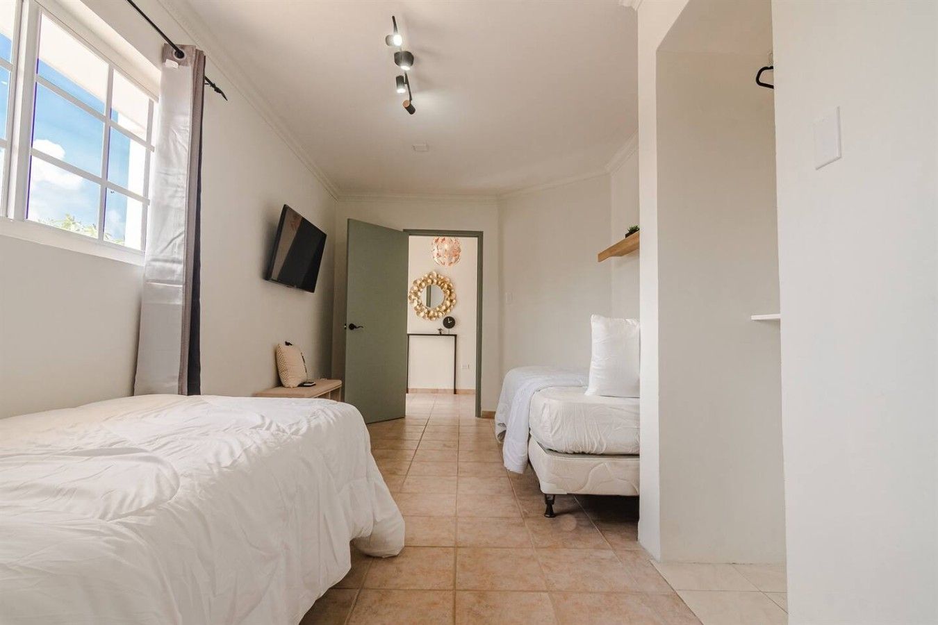 A hotel room with two beds, a TV, a mirror, and a door leading to another room.