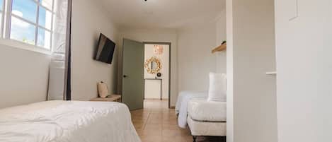 A hotel room with two beds, a TV, a mirror, and a door leading to another room.