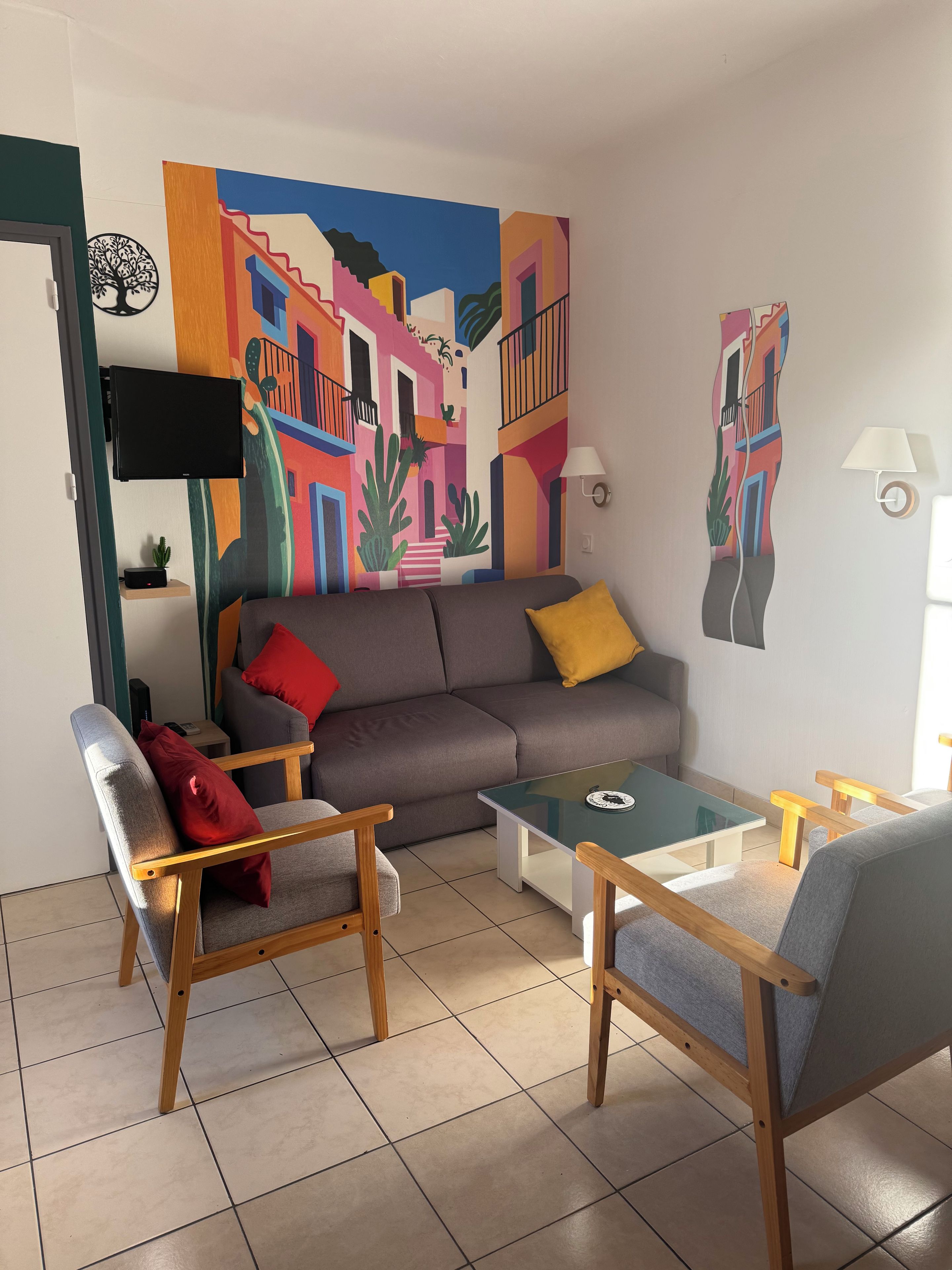 Un salon comprenant un canapé, deux fauteuils, une table basse et une fresque murale colorée.