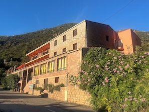 A two-story stone building with a balcony, surrounded by greenery and hills. - New Listing (Ota)