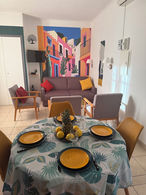 A dining area with a table set for four, a colorful mural on the wall, and a sofa in the background. - New Listing (Ota)