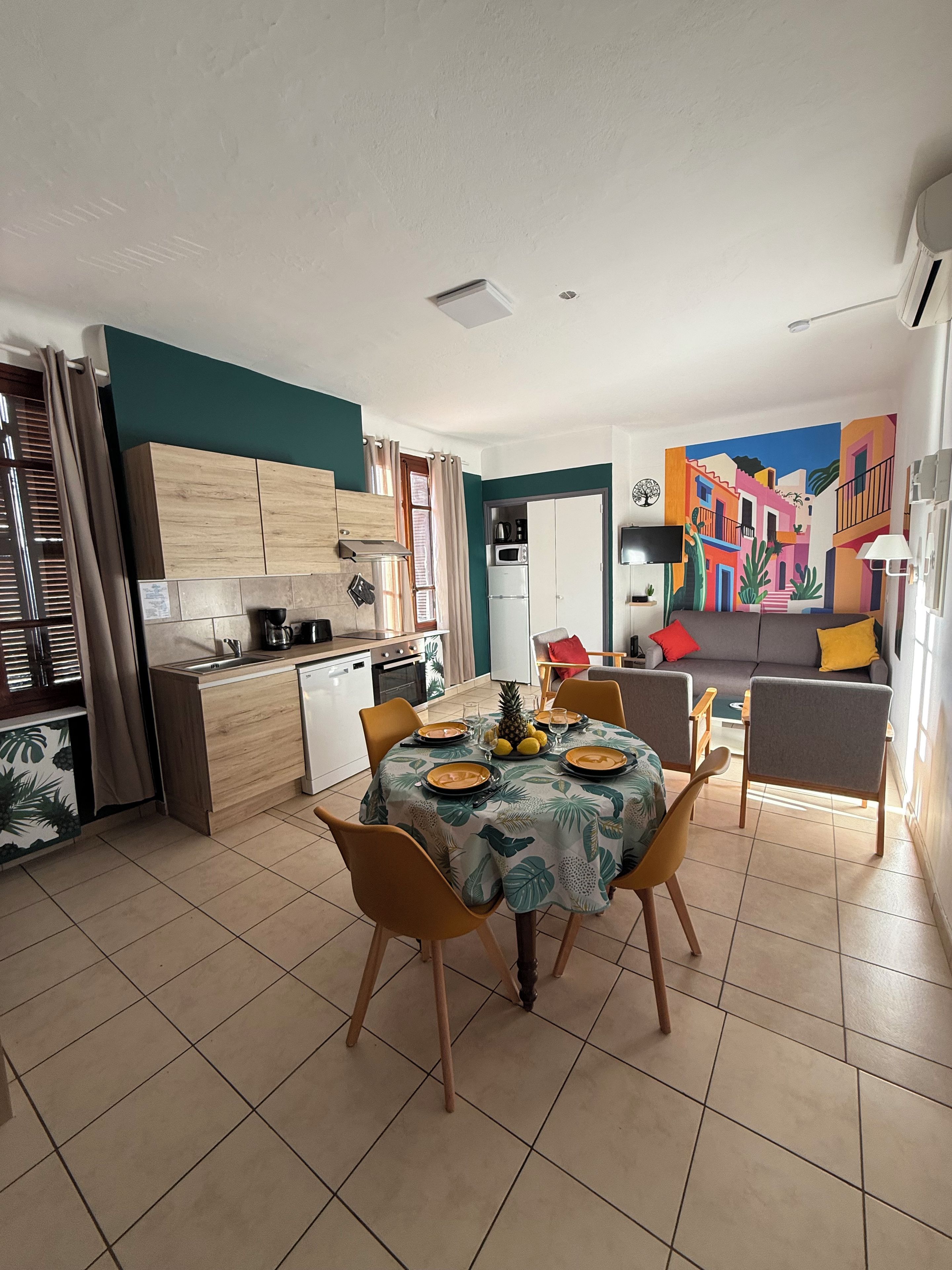 A modern kitchen with a dining area, a sofa, and a colorful mural.