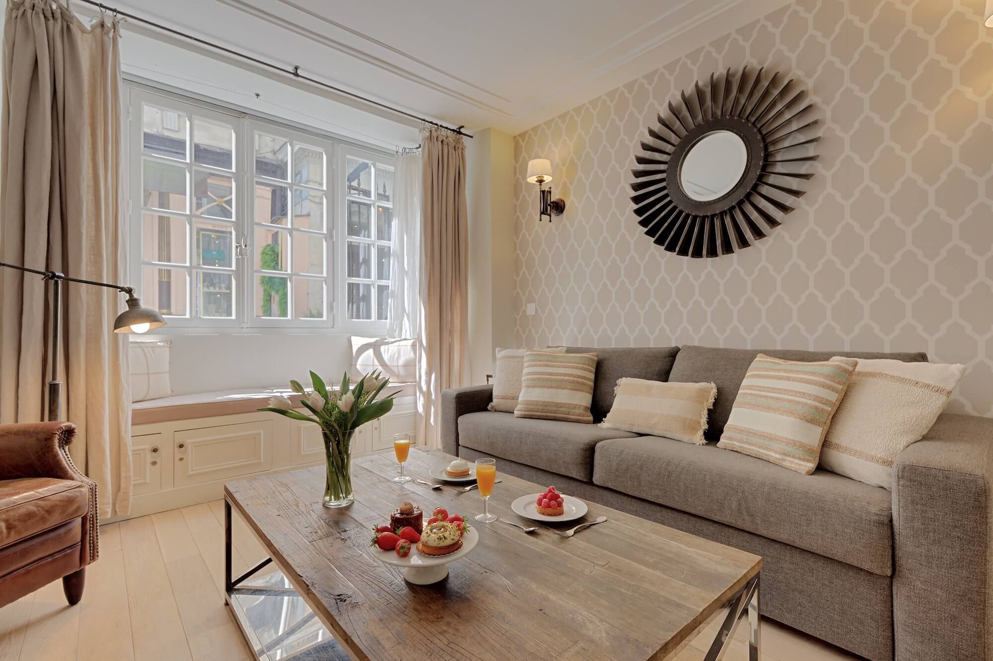 A living room with a sofa, a coffee table with food, a window with curtains, and a wall-mounted mirror.