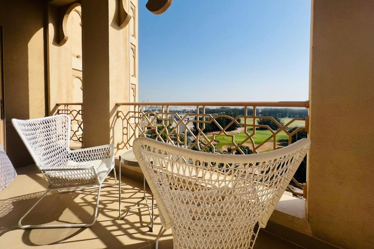 Un balcon avec deux fauteuils en osier blanc, une rambarde en métal et une vue sur un terrain de golf.