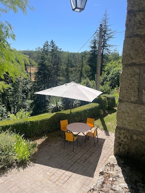 Een buitenterras met een ronde tafel, stoelen, een parasol en een stenen muur.