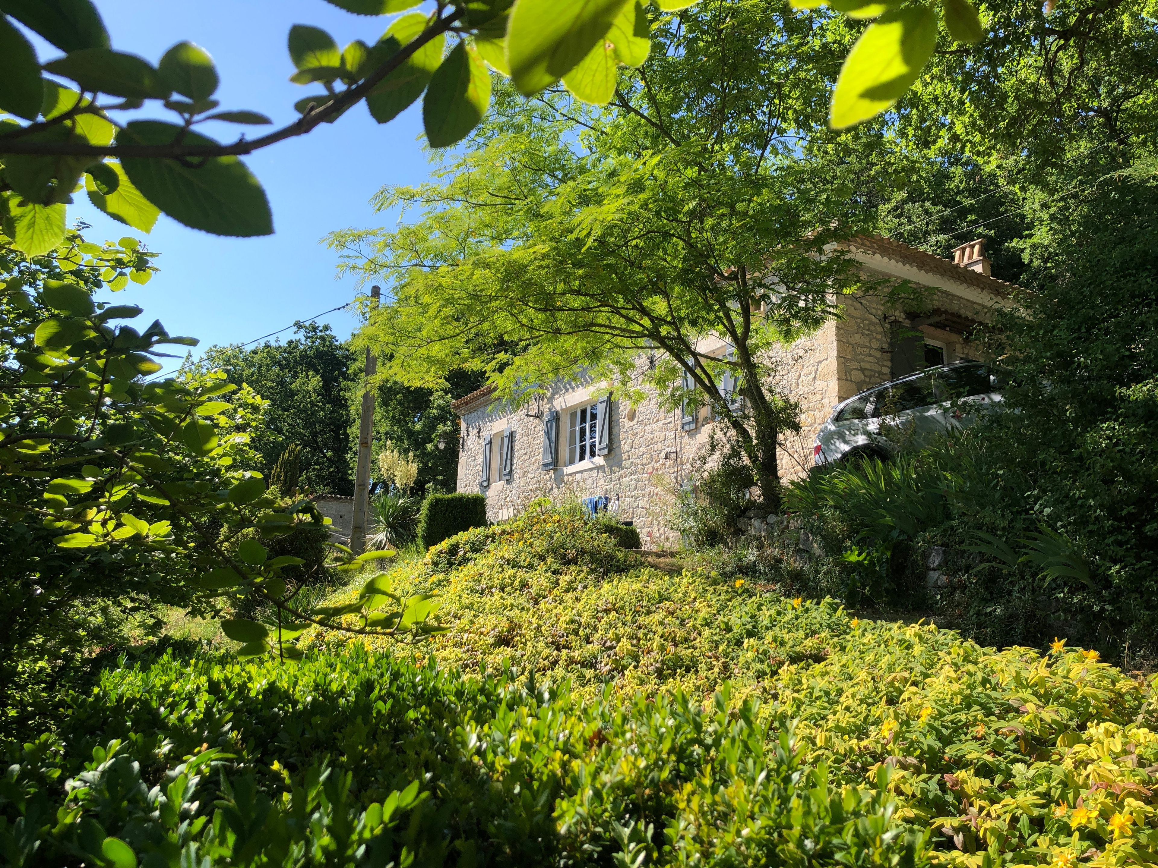 A stone building with a garden in front, surrounded by trees.