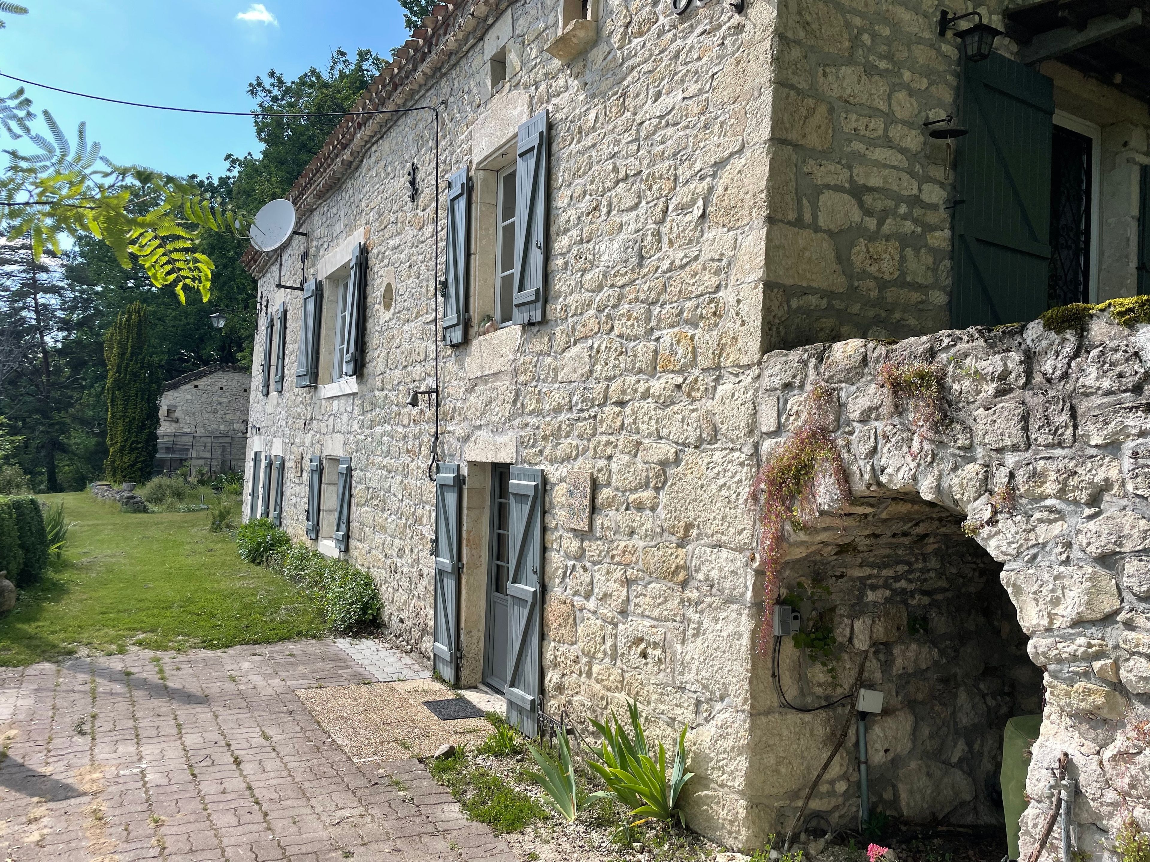 A stone building with multiple windows and shutters, a paved pathway, and a small garden area.
