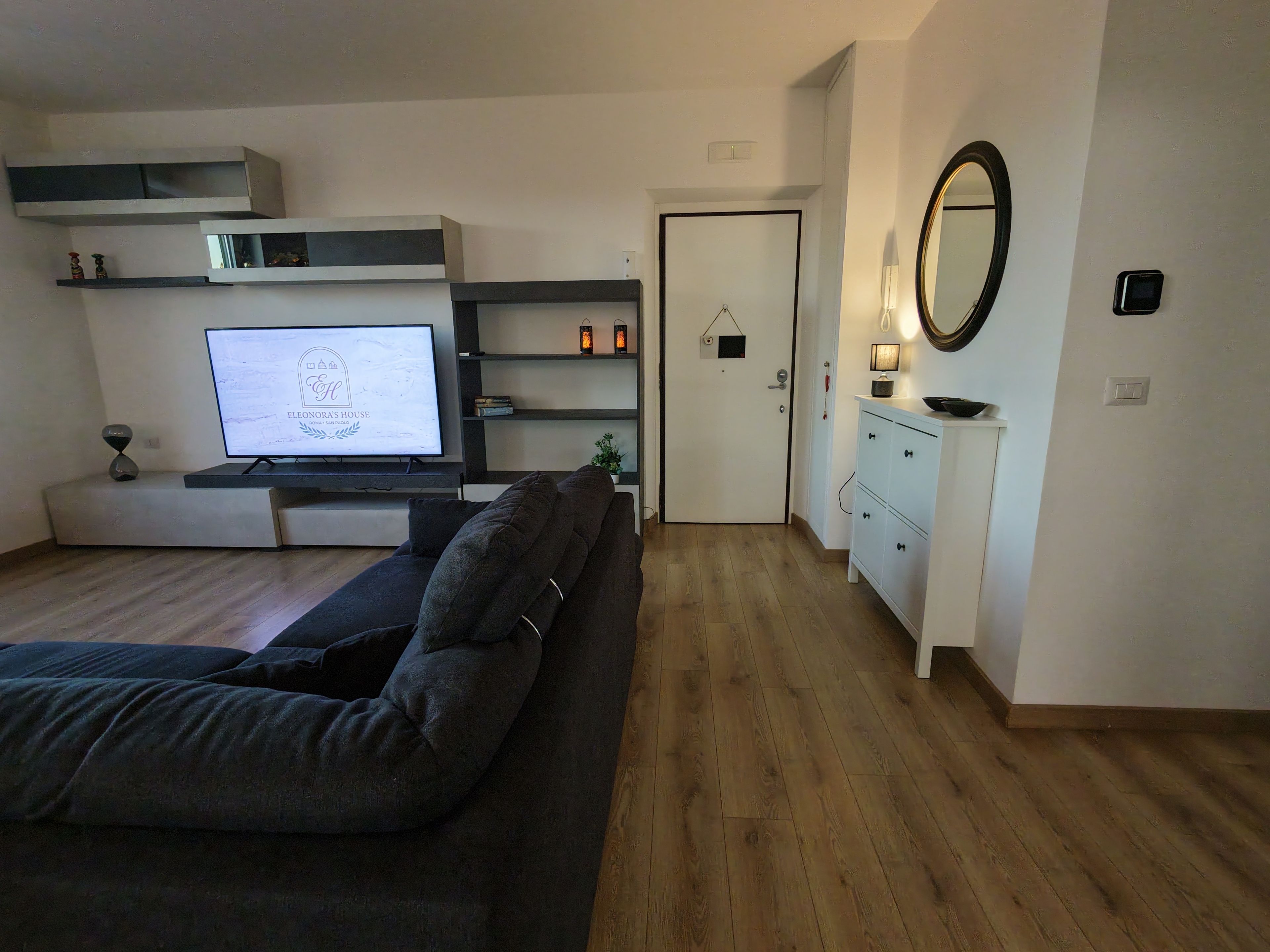 Un salon moderne comprenant un canapé, un téléviseur, des étagères et une porte donnant sur une autre pièce.
