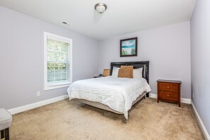 A bedroom with a bed, bedside tables, a window with blinds, a ceiling light, and a painting on the wall. - Exmoor Sunroom Retreat - 2Story Home (Jacksonville)
