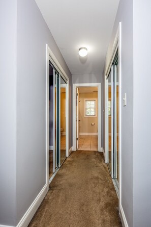 A hallway with carpeted flooring, white walls, and a ceiling light fixture.