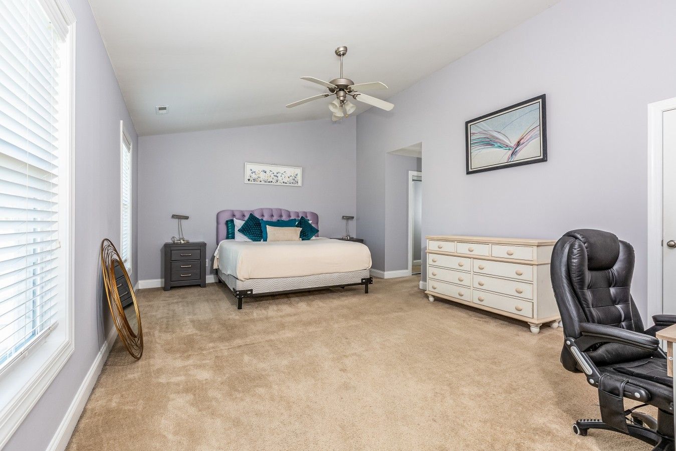 A bedroom with a bed, dresser, chair, ceiling fan, and artwork on the walls.