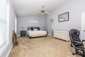 A bedroom with a bed, dresser, chair, ceiling fan, and artwork on the walls.