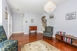 A spacious living room with hardwood flooring, a chandelier, a bookshelf, and a staircase leading to another level. - Exmoor Sunroom Retreat - 2Story Home (Jacksonville)