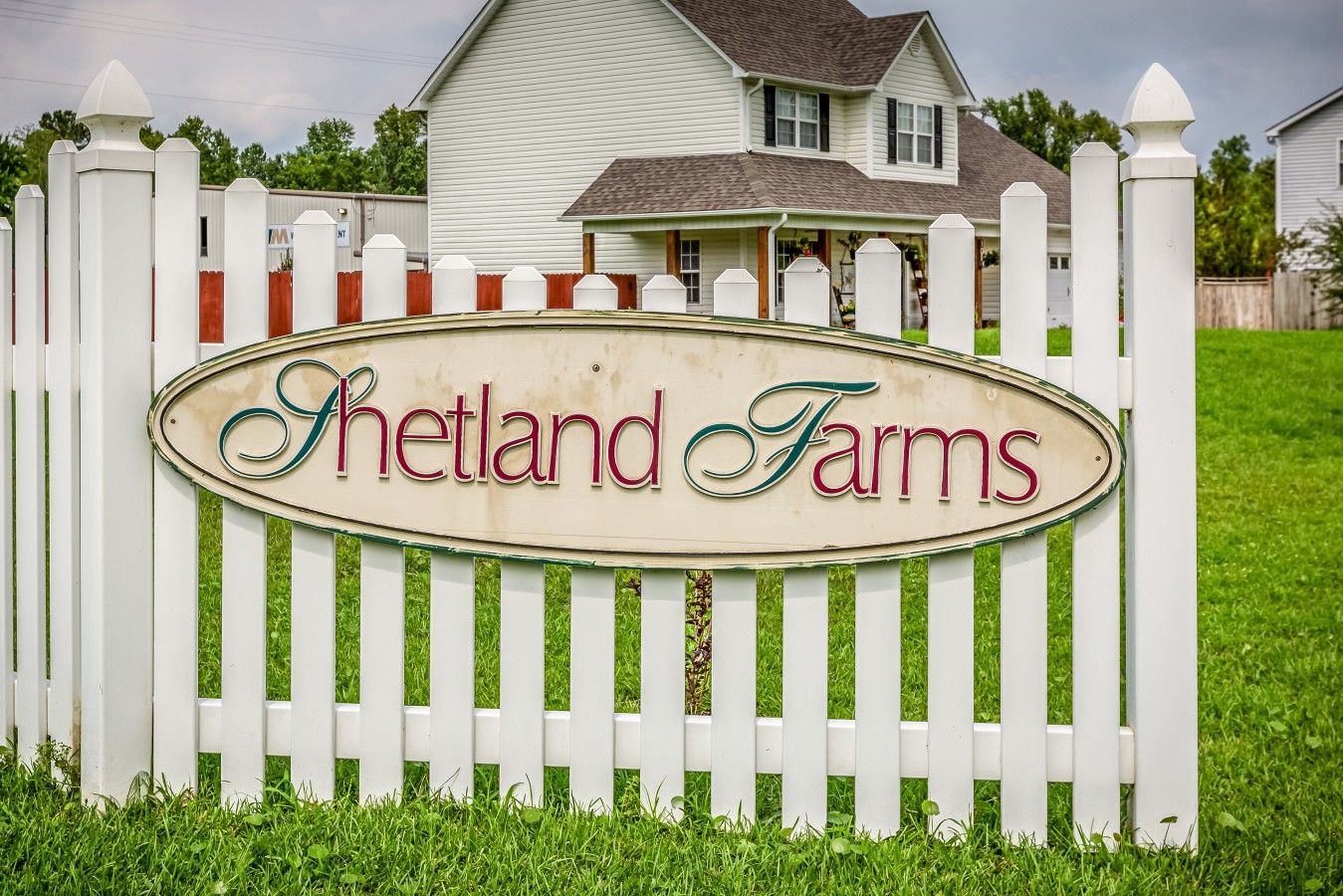 A white picket fence with a sign that reads 'Hetland Farms' in front of a house.
