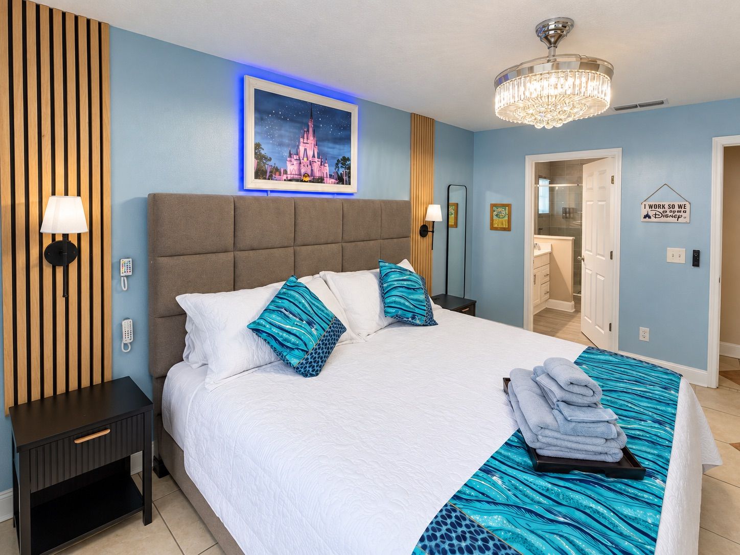 Une chambre d’hôtel avec un grand lit, un lustre, un tableau encadré représentant un château et un panneau accroché au mur.