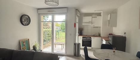 A living room with a sofa, a dining table with chairs, a kitchen area with cabinets, and a sliding glass door leading to a patio.