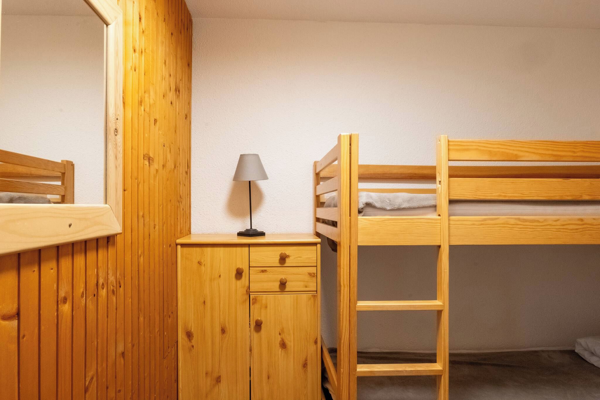 A bunk bed with a ladder, a bedside table with a lamp, and a wooden wardrobe.