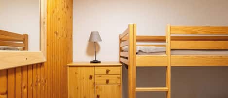 A bunk bed with a ladder, a bedside table with a lamp, and a wooden wardrobe.