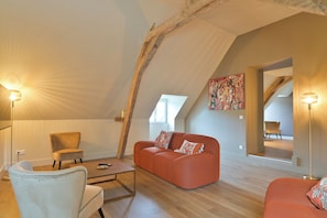A cozy loft-style room with a sloped ceiling, a red sofa, a white armchair, and a small coffee table. - New Listing (Beaumont-en-Véron)