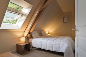 A bedroom with a sloped ceiling, a bed with white bedding, two bedside lamps, and a window with a view of greenery. - New Listing (Beaumont-en-Véron)