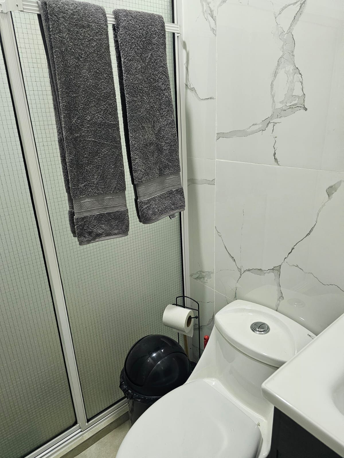 Un baño con ducha, inodoro y un cubo de basura negro.