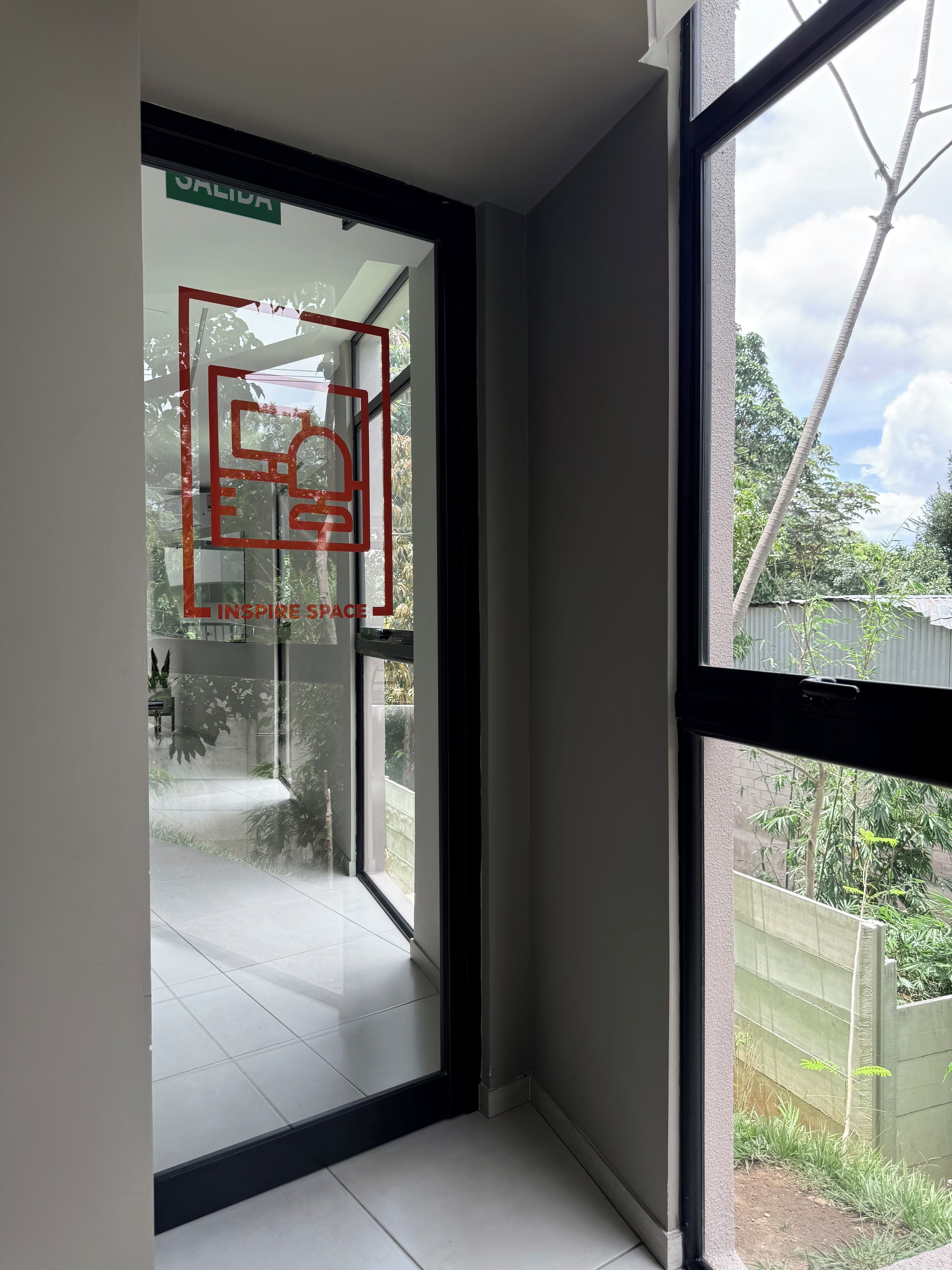 A room with a large window, a door with a sign, and a view of a garden.