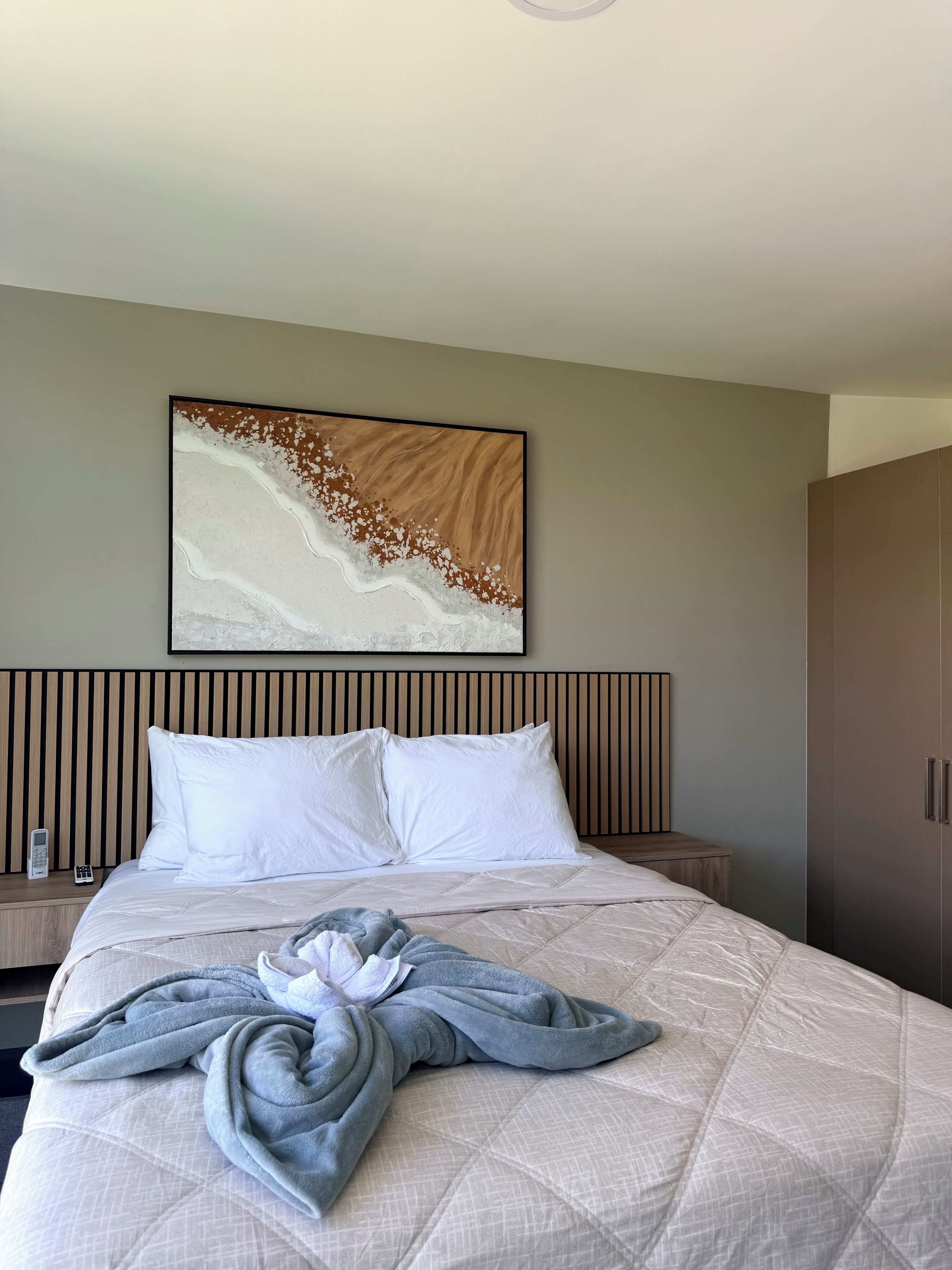 A hotel room with a bed, a wall-mounted artwork, a wardrobe, and a bedside table with a phone.