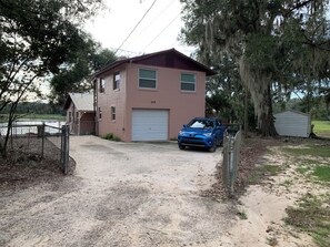 En tvåvåningsbyggnad med ett garage, en blå SUV parkerad framför och ett inhägnat område med en brygga.