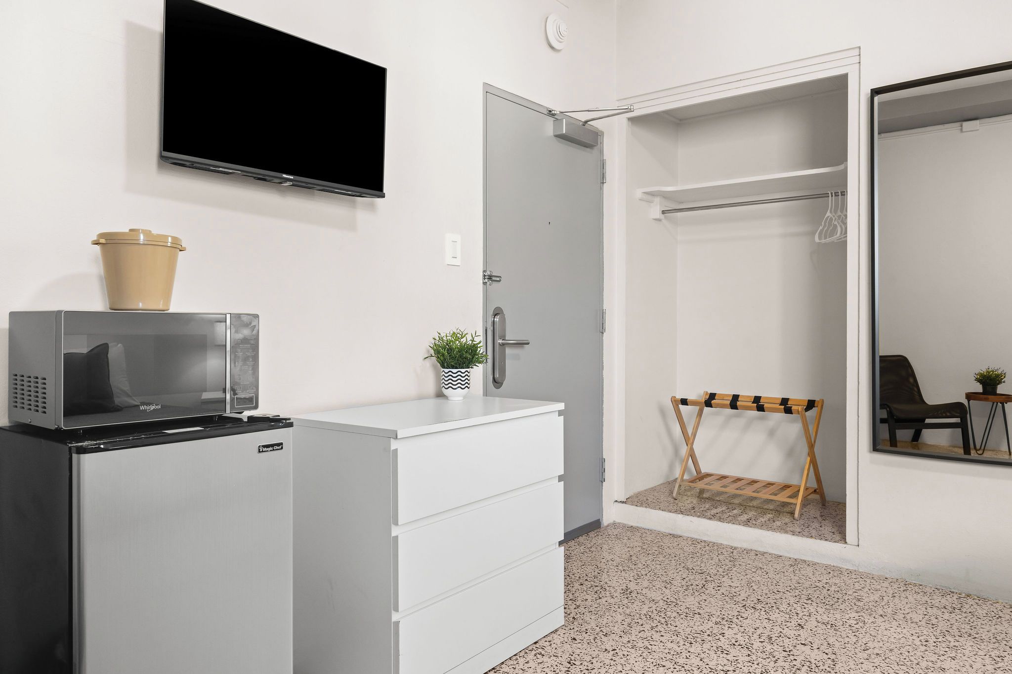 A hotel room with a kitchenette, a flat-screen TV, a wardrobe, and a small seating area.
